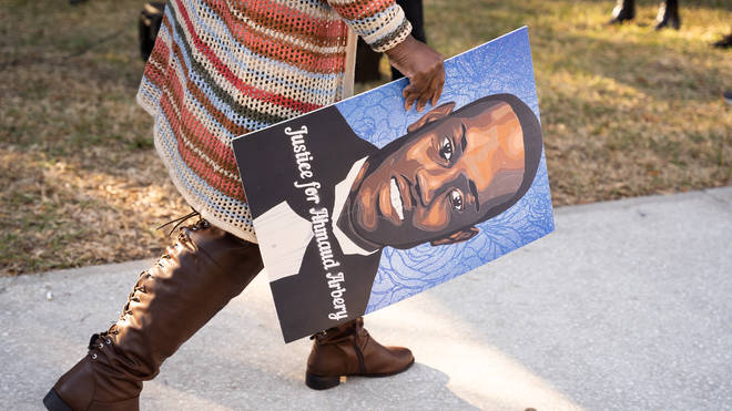 A woman carries a portrait of Ahmaud Arbery outside the Glynn County Courthouse as the jury deliberates in the trial of the killers of Ahmaud Arbery